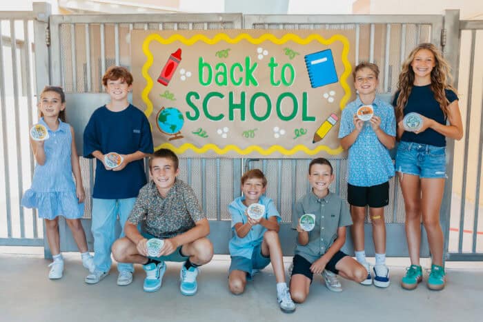 Group of smiling kids holding ¡Yo Quiero! Grab & Go dips in front of a colorful “Back to School” sign.