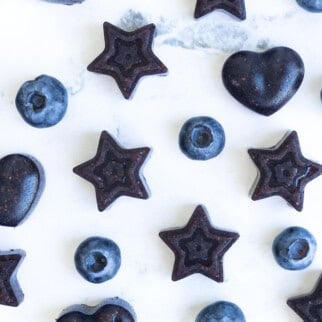 Close-up of homemade blueberry gummies shaped like stars and hearts with fresh Consalo blueberries.
