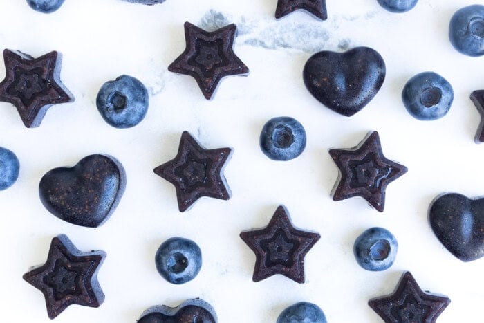 Close-up of homemade blueberry gummies shaped like stars and hearts with fresh Consalo blueberries.