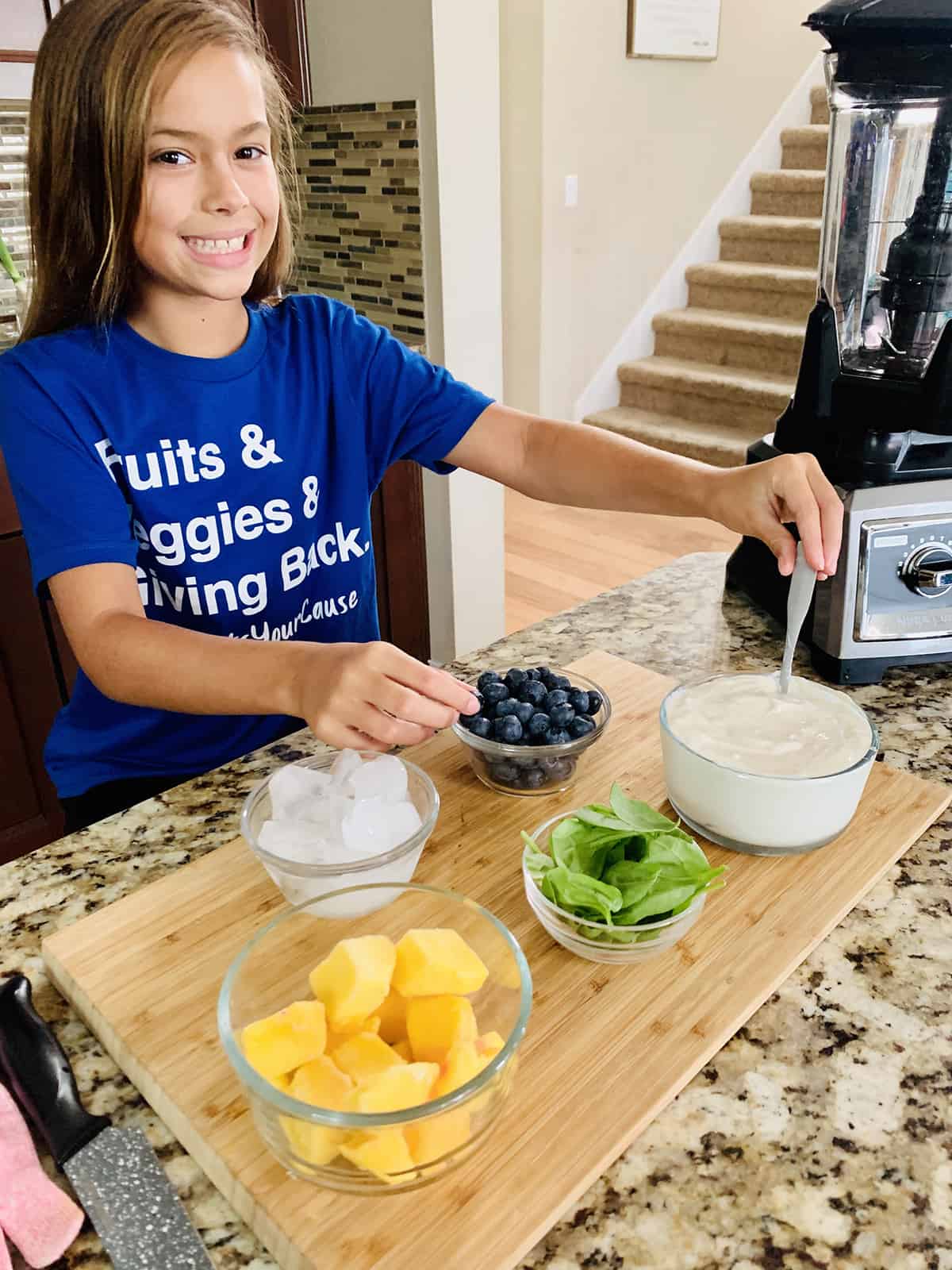 A little girl is preparing a Banana, Blueberry, and Mango Smoothie in a mixer.