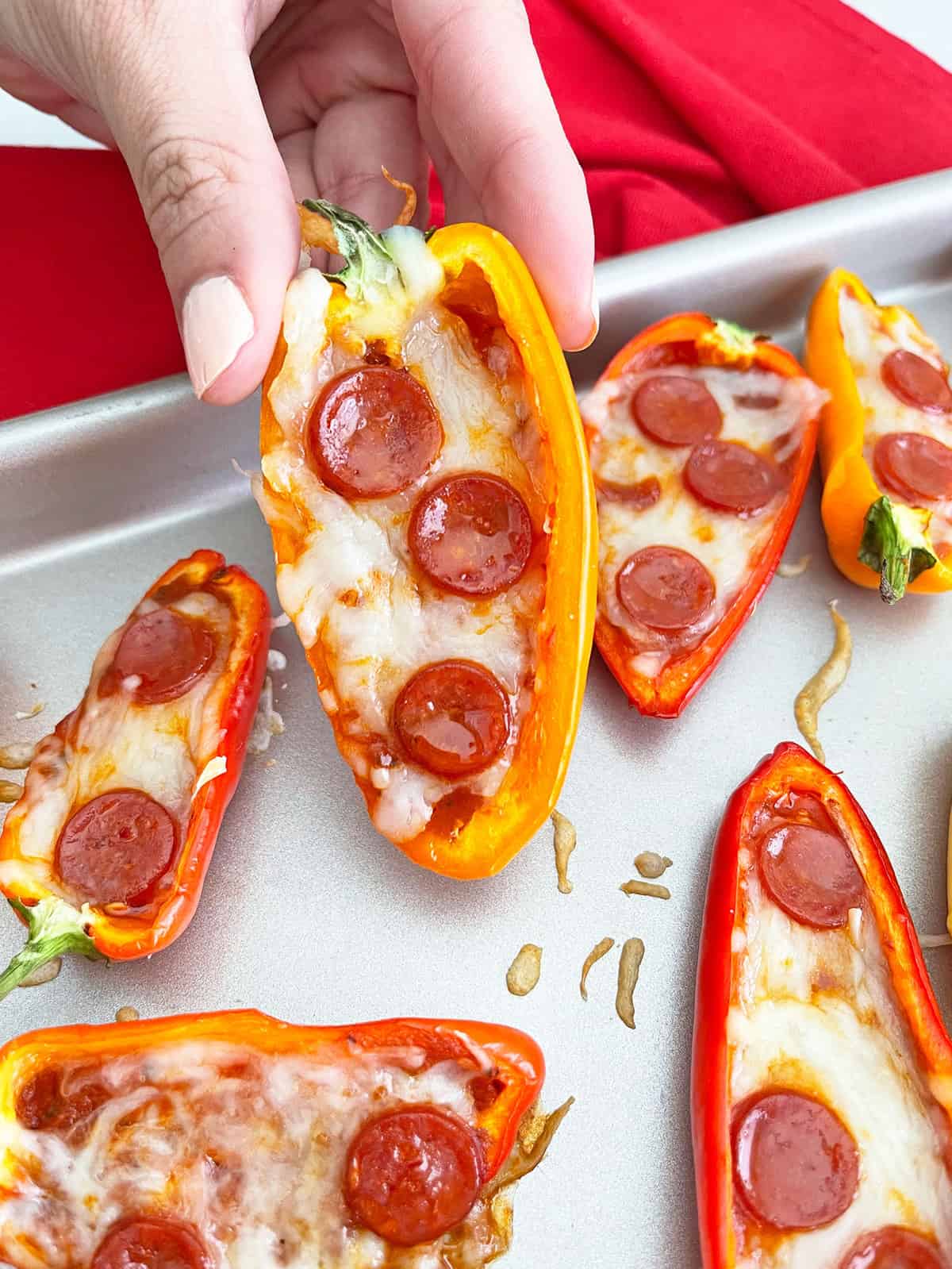 Close up of hand picking up mini pepper pizza off baking sheet.