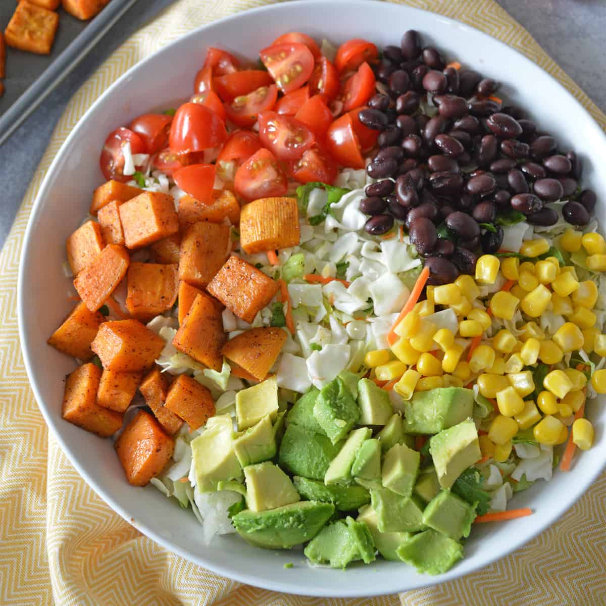 White bowl with black beans, corn, avocado, roasted sweet potatoes and tomatoes sectioned out.
