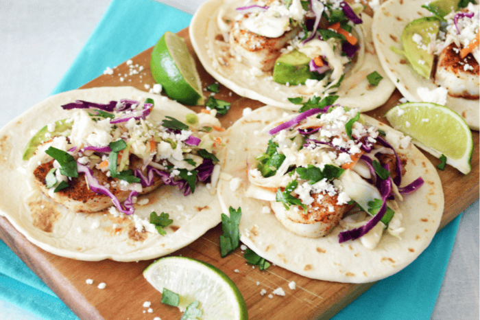 Baked fish tacos with slaw and cilantro served on a wooden board, with some limes on the side.