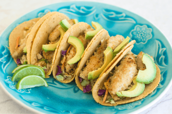 Baja-style tacos recipe served on a dish with avocado as a topping and a few limes on the side.